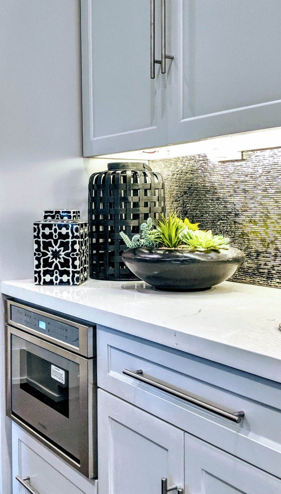Bellaire Estate — A detail of the kitchen’s shimmering metallic backsplash, soft gray cabinetry, and integrated stainless appliances.