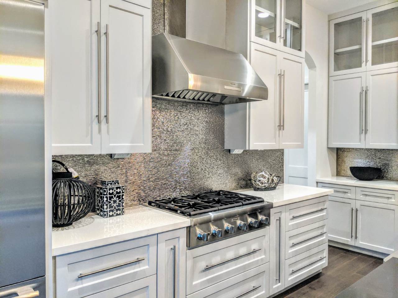 Bellaire Estate — The wider kitchen view, with glass-front uppers and the metallic backsplash carrying across the cooking wall.