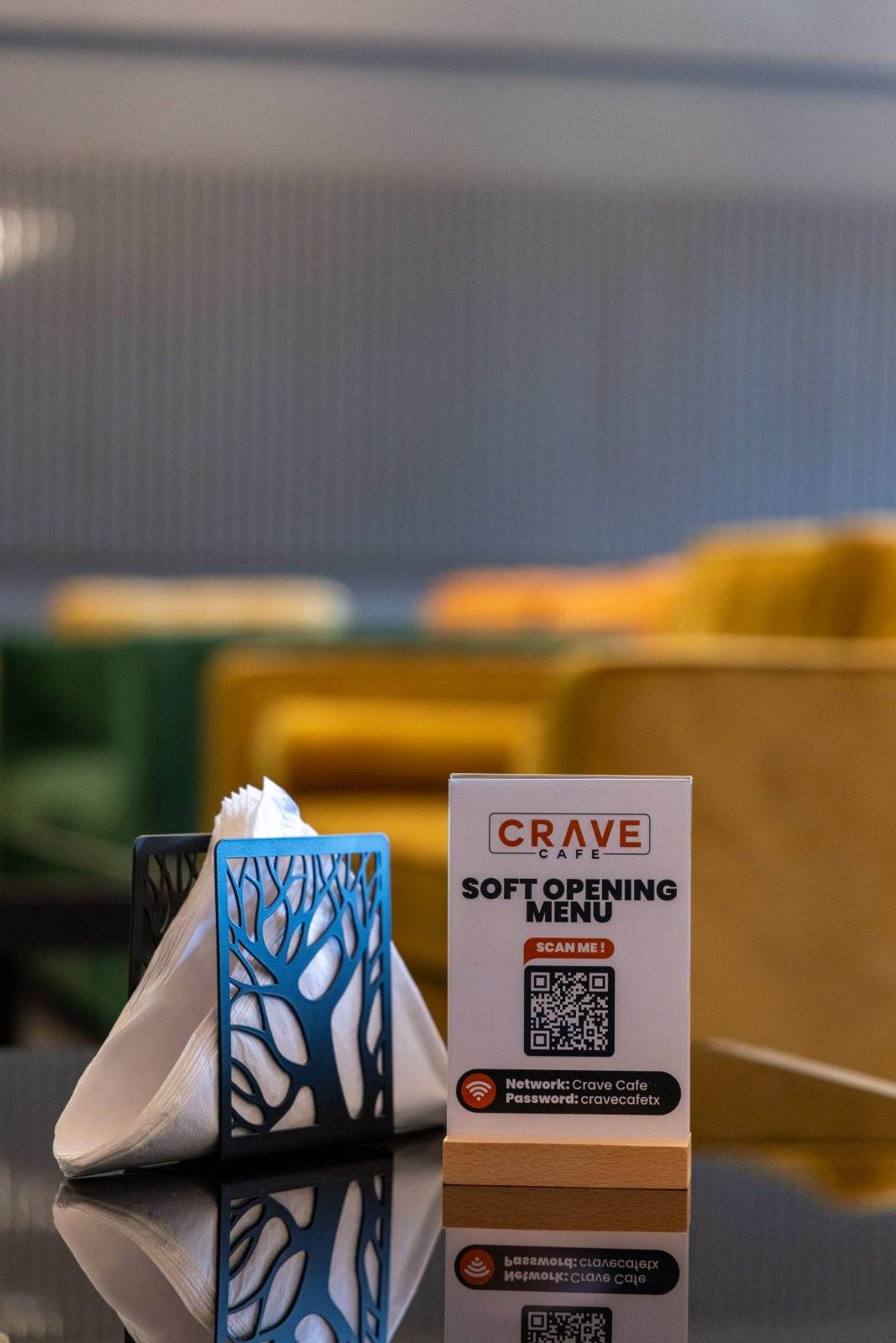 Crave Café — Tabletop detail: a laser-cut tree napkin holder and branded menu card on a glossy black table.