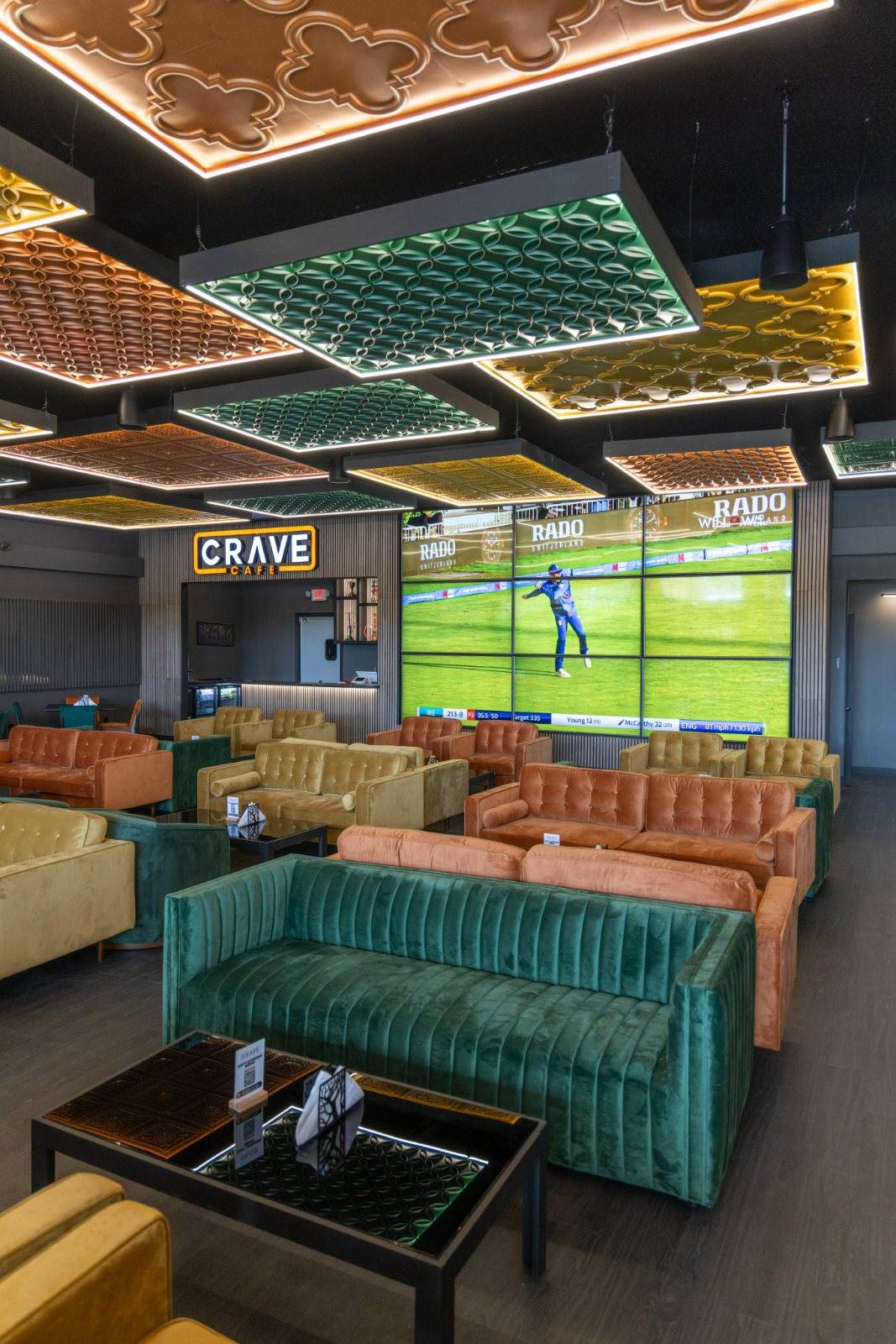 Crave Café — The room in full — rows of jewel-toned velvet sofas arranged around the central video wall.