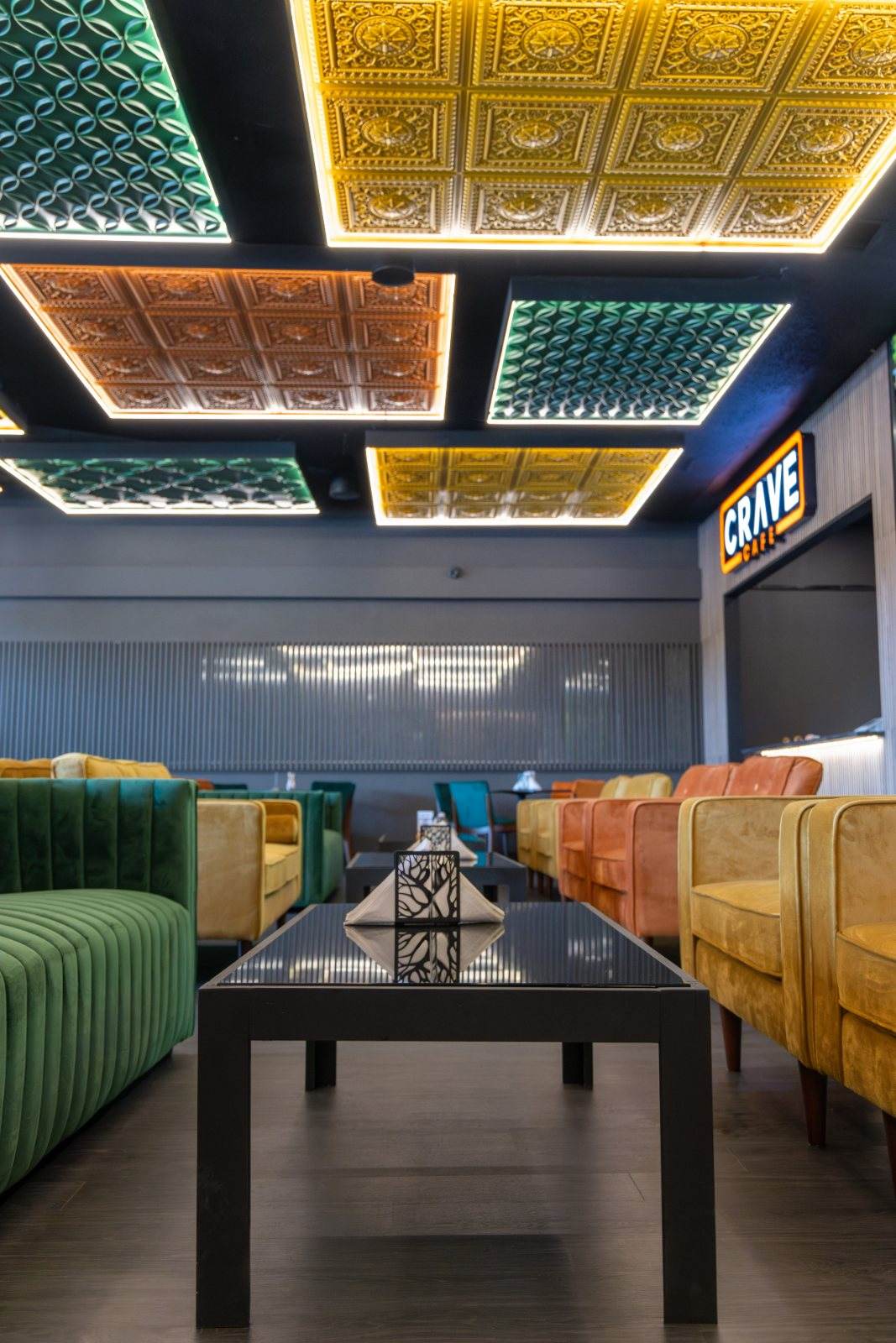 Crave Café — A wide aisle between green and gold velvet seating draws the eye toward the bar.