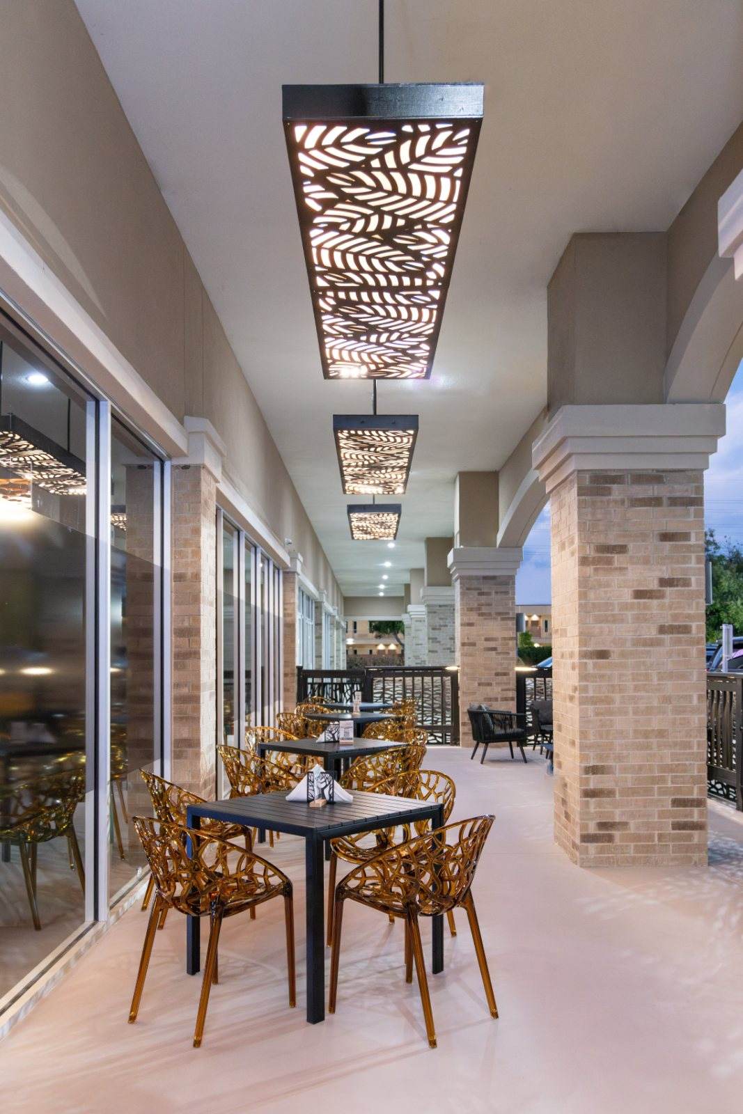 Crave Café — The covered patio: amber sculptural chairs and leaf-cut pendant lights between brick columns.