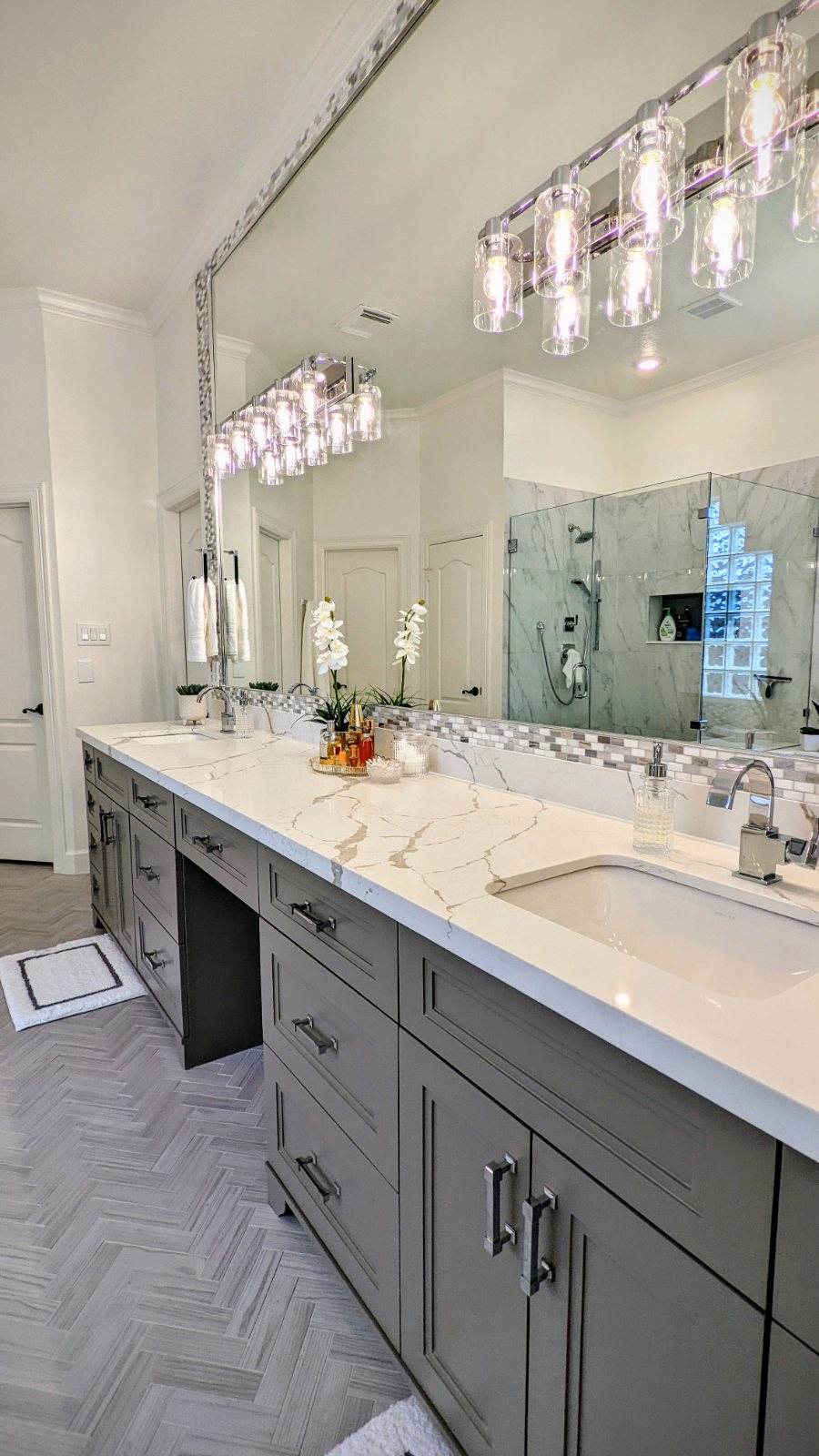 Lakes of Parkway Residence — The primary bath’s showpiece: a custom gray double vanity in veined quartz beneath a row of glass-cylinder sconces.