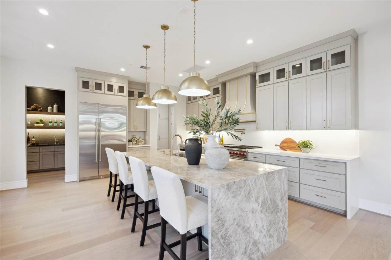 West University Custom Home — Custom kitchen with waterfall island, brass pendants, and pro range